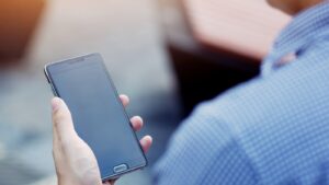 Dark screen of a mobile phone screen viewed over the shoulder of a man about to make a call