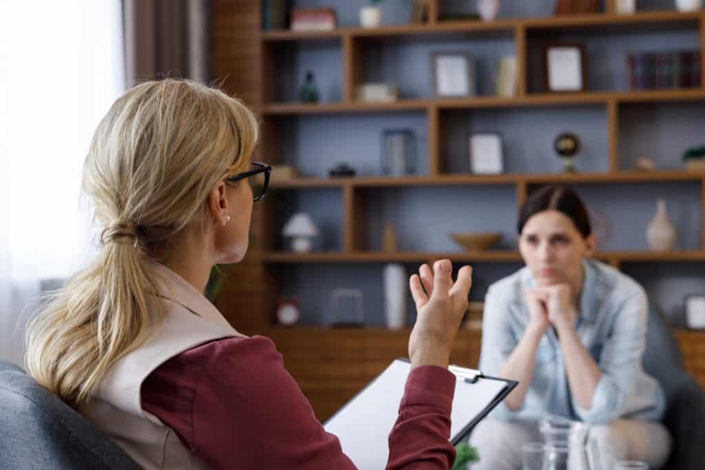 Over shoulder view of female psychologist sitting in armchair, talking with patient
