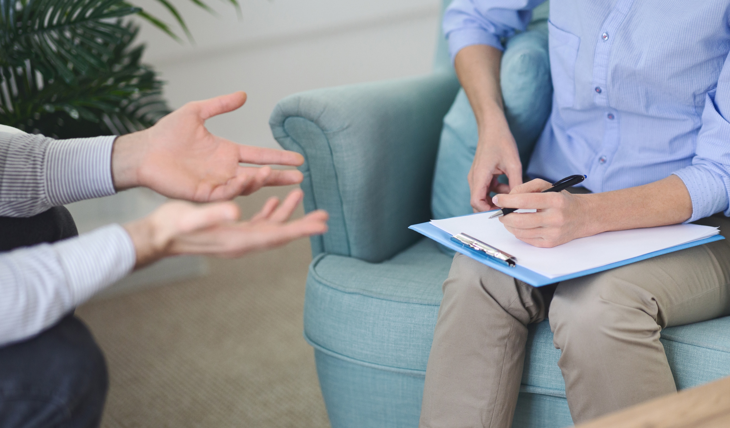 Cropped image of therapist actively listens while taking notes on a clipboard, during a counseling session with man in a modern office on a sunny afternoon 