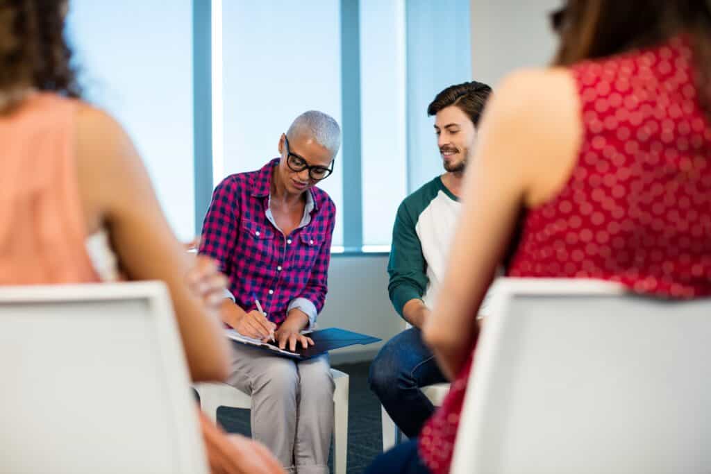 woman writing on a notepad while in group therapy