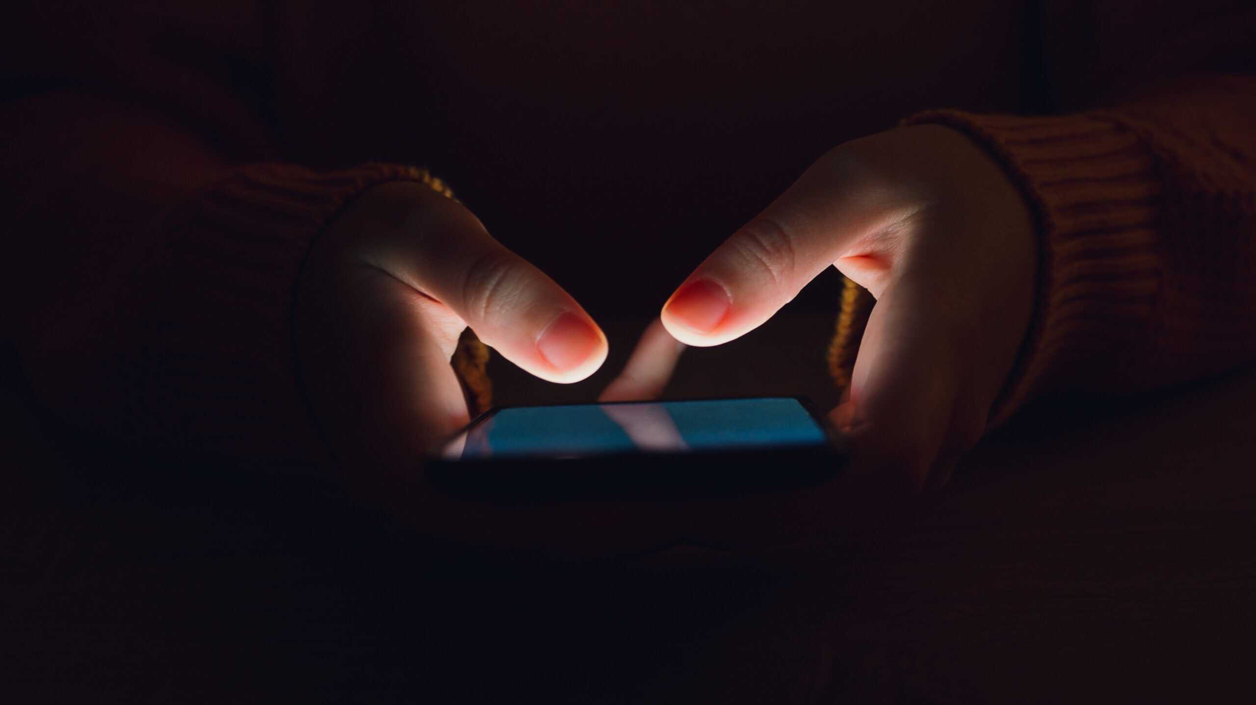 woman's hands close shot, using smartphone in the dark