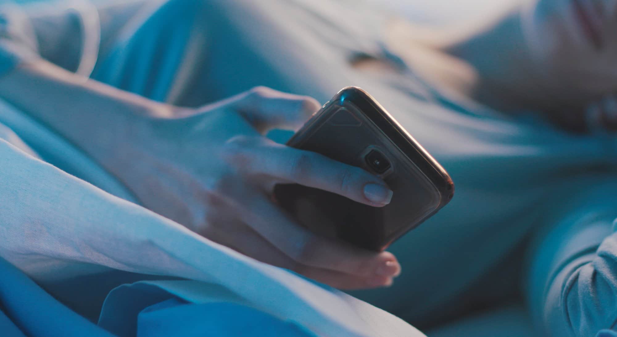 using mobile phone in bed, discreet image of a woman checking her phone while in bed